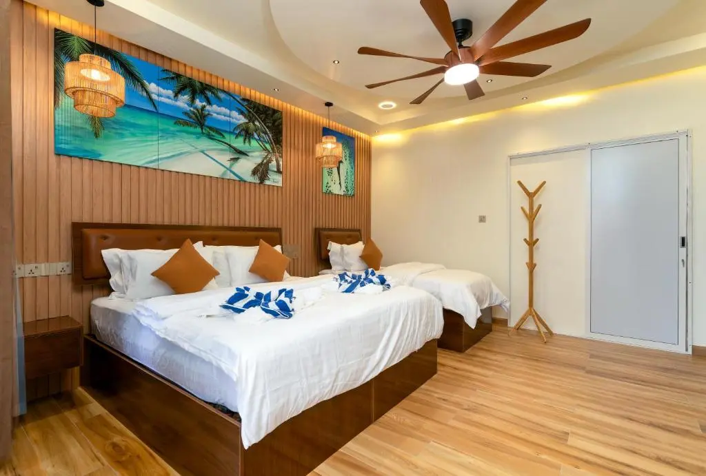 Double guest room with wooden floor and beach wall art at Hidden Tide Villa, Ukulhas Island, Maldives