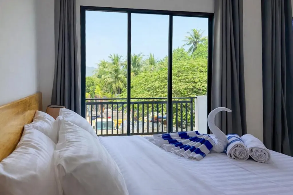 Guest room bed with towel art and a palm-view window at Hiraya Guesthouse, Ukulhas Island, Maldives