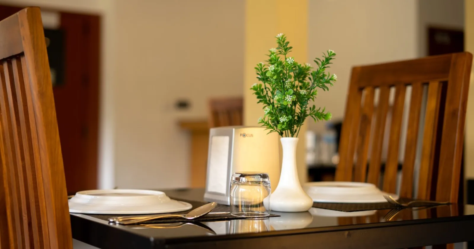 A set table with wooden chairs, white plates and a small vase of greenery at Nala Bistro, Ukulhas Island, Maldives