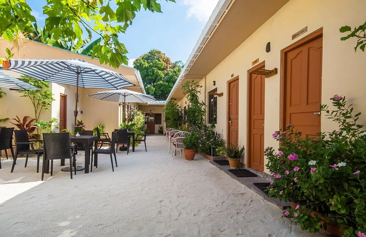 Sandy courtyard with cafe tables, umbrellas and flowers at Paguro Villa, Ukulhas Island, Maldives