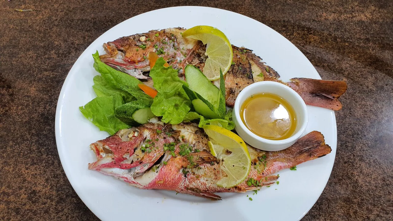 Two whole grilled reef fish plated with salad, lemon and a dipping sauce at Peperone Restaurant, Ukulhas Island, Maldives
