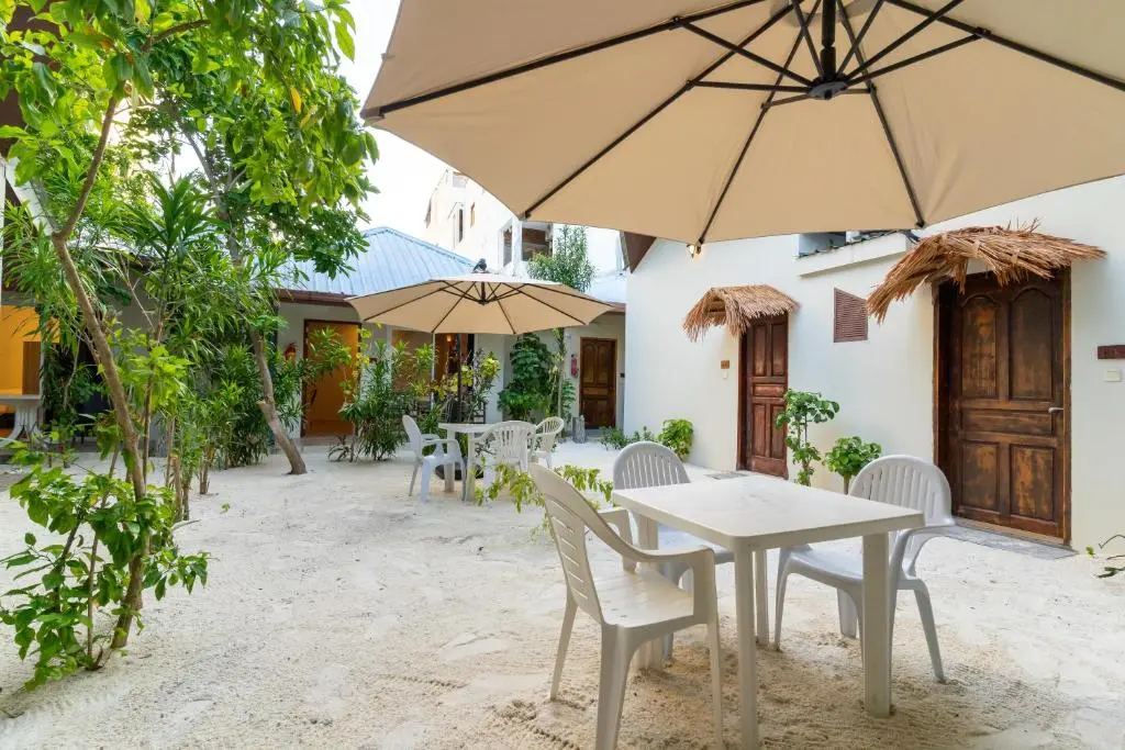 Sandy garden courtyard with parasols and outdoor tables at Villa Crescenta, Ukulhas Island, Maldives